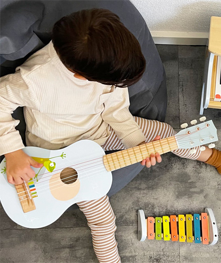 Kleines Kind spielt auf der akustischen Holzgitarre zur musikalischen Früherziehung nach Montessori